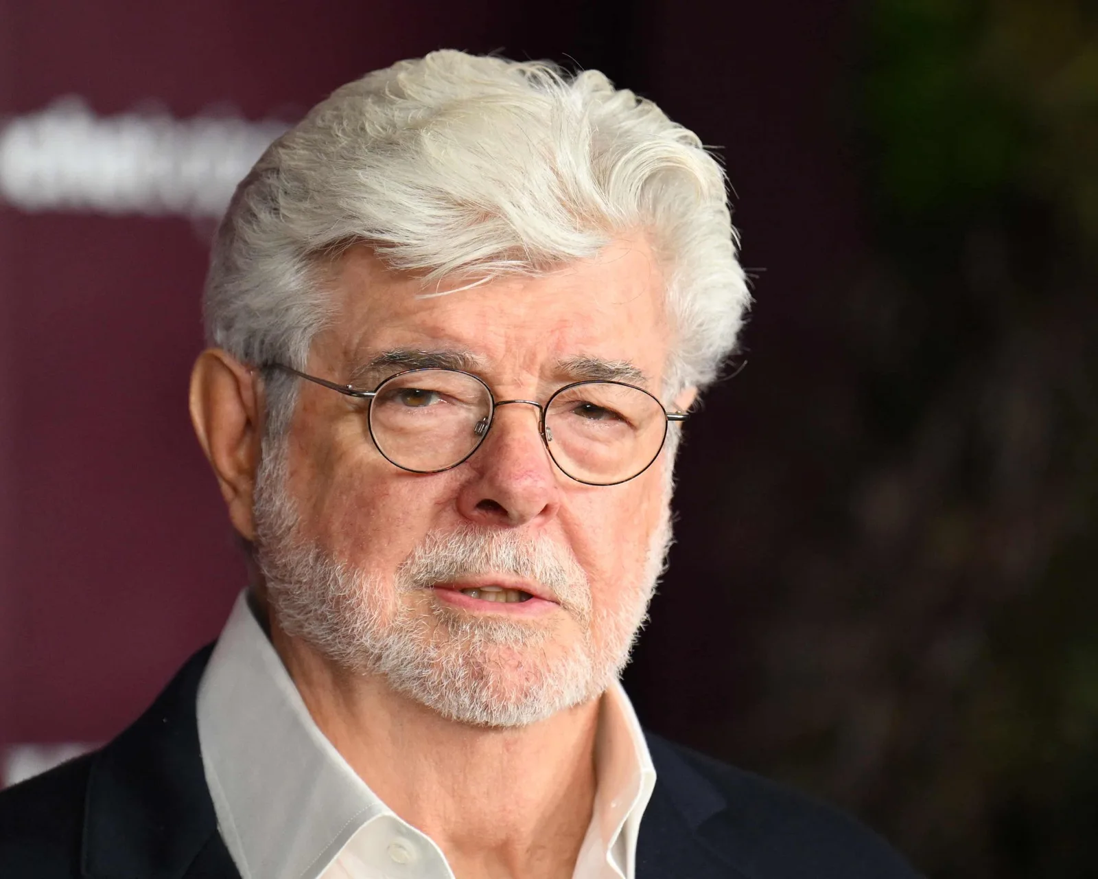 Close-up of George Lucas in round glasses and a dark jacket at a red-carpet event.